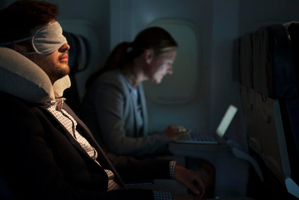 Man sleeping on a plane while someone works beside him